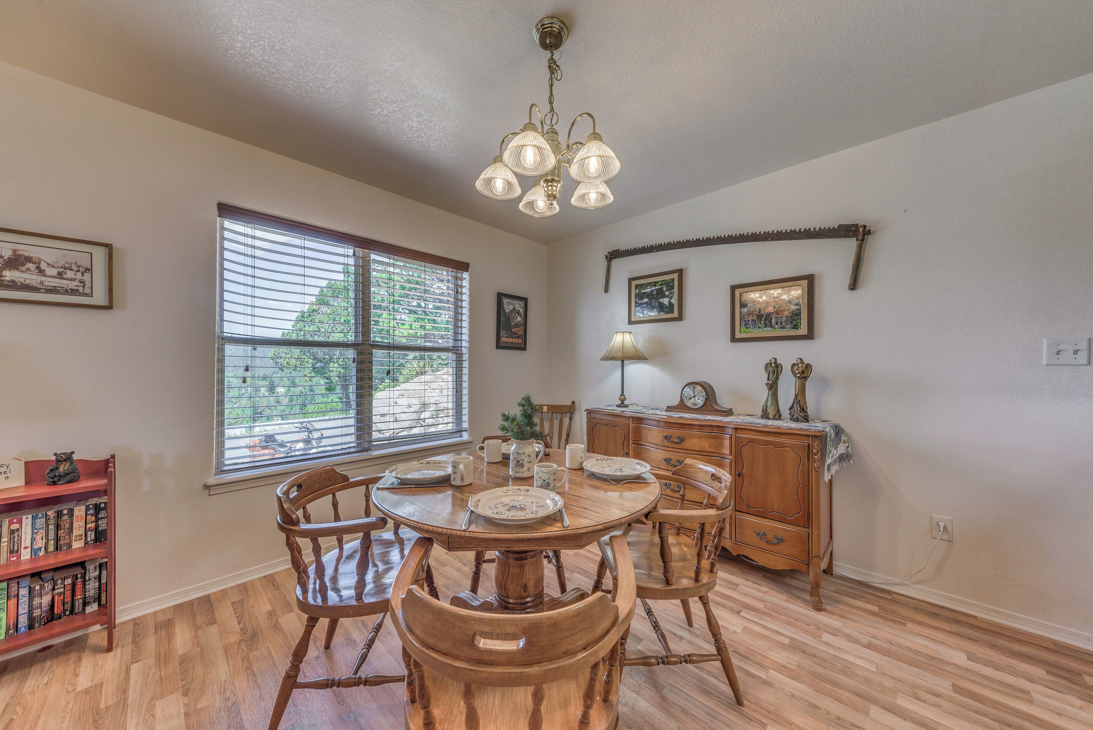 A dining area with a wooden table and chairs, a chandelier, and a window with blinds.
