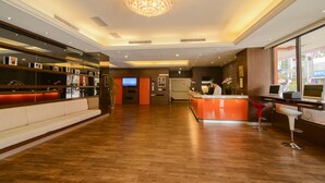 Um saguão de hotel com balcão de recepção, área de estar e televisão.