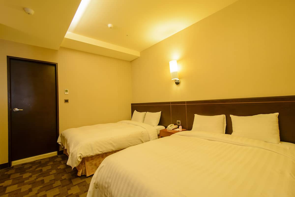 A hotel room with two beds, a dark door, a wall-mounted phone, and a ceiling light.
