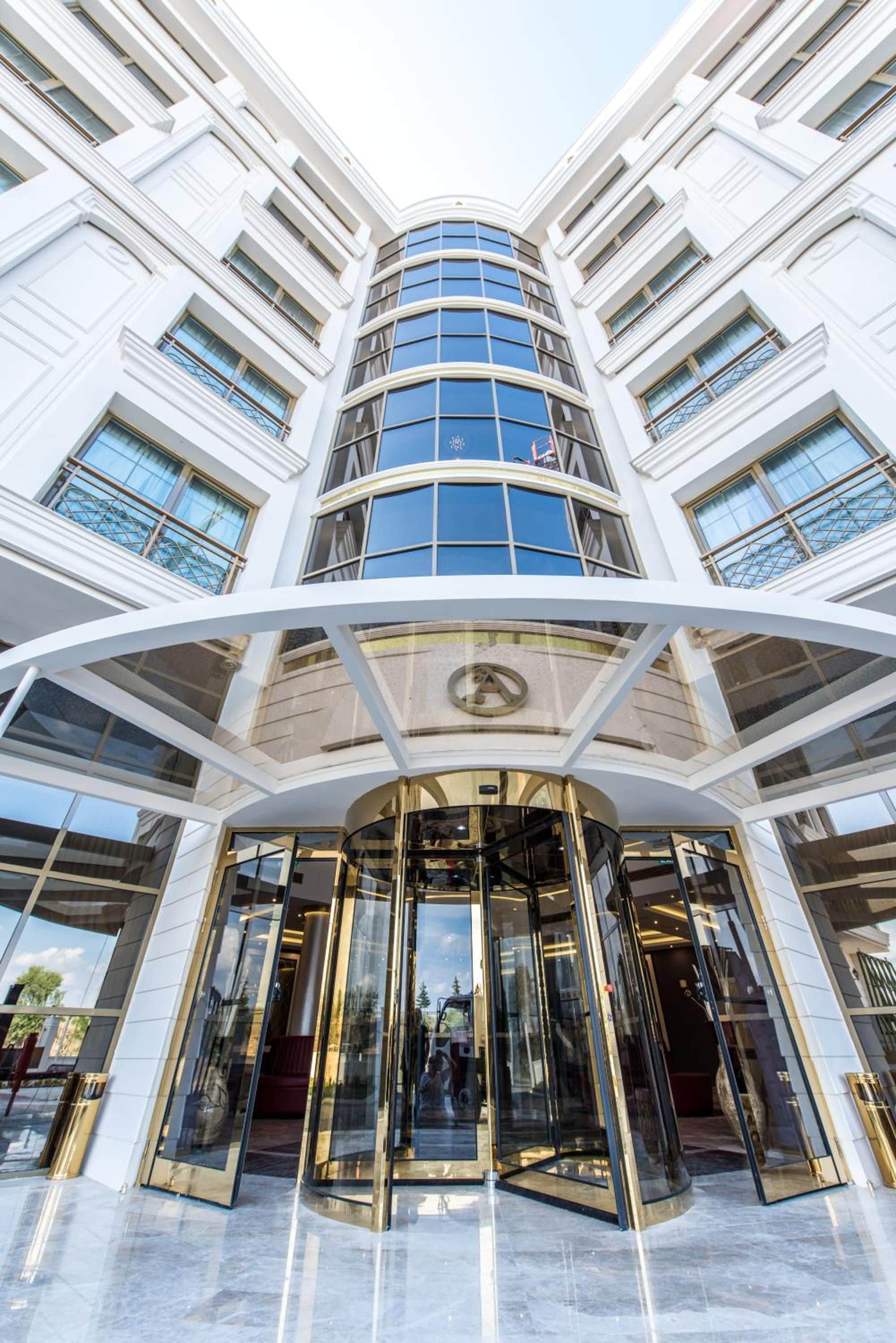 A modern building with a curved entrance, large glass windows, and a prominent logo above the doors.