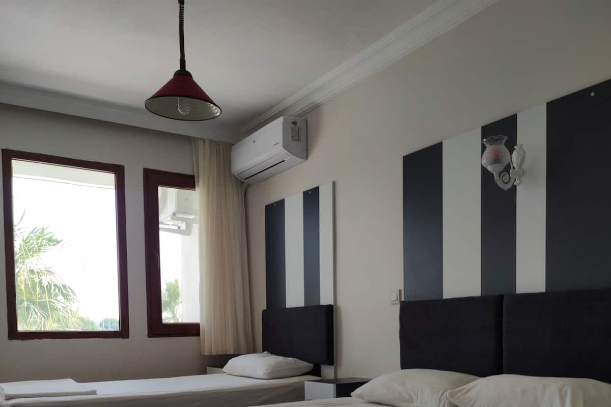 A hotel room with two beds, a ceiling fan, an air conditioning unit, and a window with curtains.