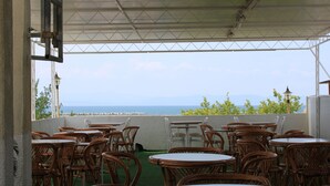 Un área de estar al aire libre con mesas y sillas de mimbre, con vistas panorámicas al mar y a las montañas.