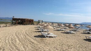 Una playa con tumbonas y sombrillas, una pequeña cabaña y un cielo despejado.