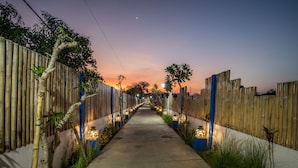 A pathway flanked by bamboo fences and illuminated by decorative lights, leading towards a distant point. - Santorini Beach Resort (Gili Trawangan)