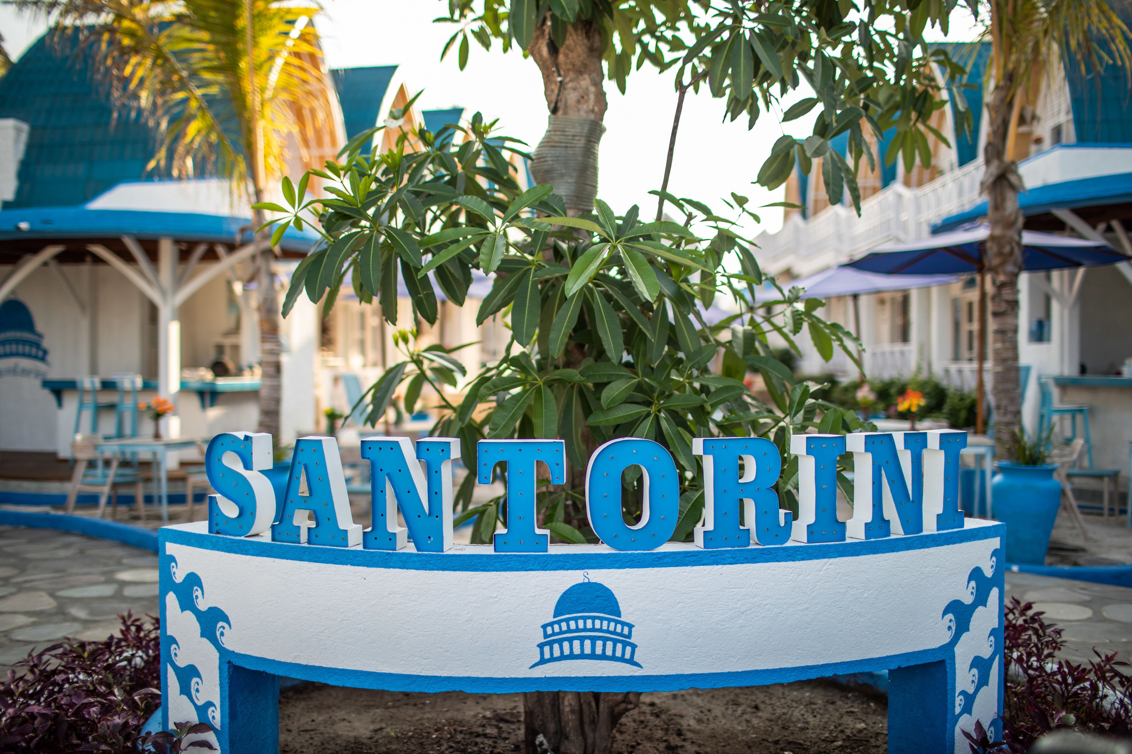 A sign with the name 'SANTORINI' in large letters, a dome symbol, and a blue and white color scheme.