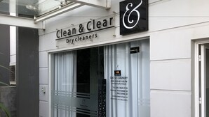 A storefront with a sign reading "Clean & Clear Drycleaners" and a sign for "Giati Hill Laundry" with operating hours and contact information.