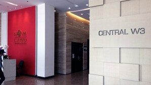 A modern hotel lobby with a red wall featuring the Nova Land logo, a reception desk, and a sign for Central W3.
