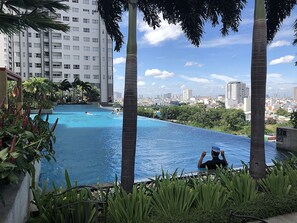 A swimming pool with a cityscape in the background, surrounded by palm trees and greenery. - Sunrise City Luxury New 2bed2bath SW POOL1 (Ho Chi Minh City)