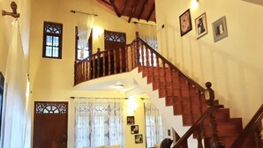 Uma sala de estar ampla, com teto alto, escada de madeira e sofá branco.
