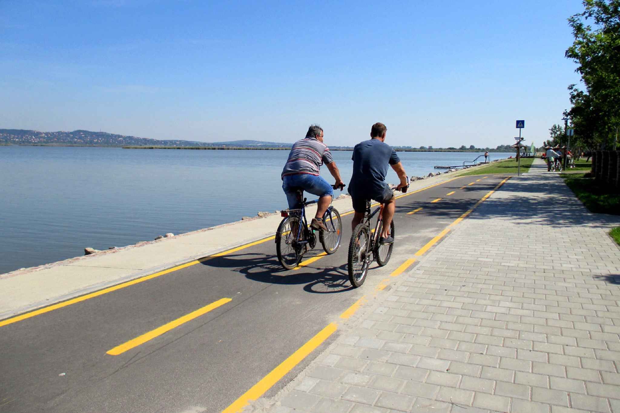 Two people riding bicycles on a paved path alongside a body of water.