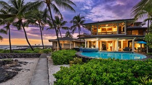 A two-story beachfront property with a swimming pool, palm trees, and a view of the ocean at sunset. - 🏖️Gorgeous Ocean Front Estate | Gated Community | Walk to Town (Kailua Kona)