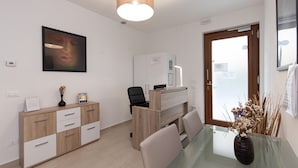 A modern office space with a wooden desk, a black office chair, a glass table, and a vase with dried plants. - San Polo Star (Venice)