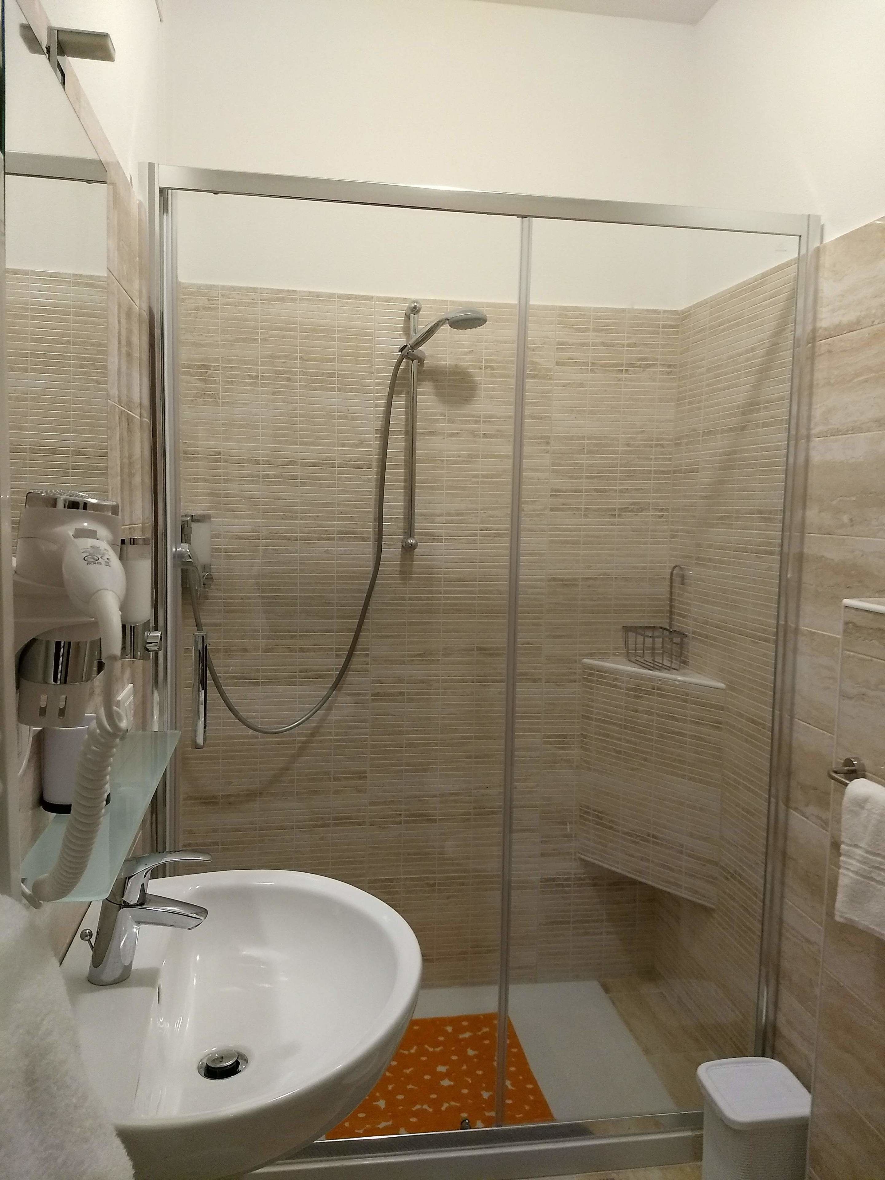 Ein Badezimmer mit Duschkabine, weißem Waschbecken und Handtuchhalter.