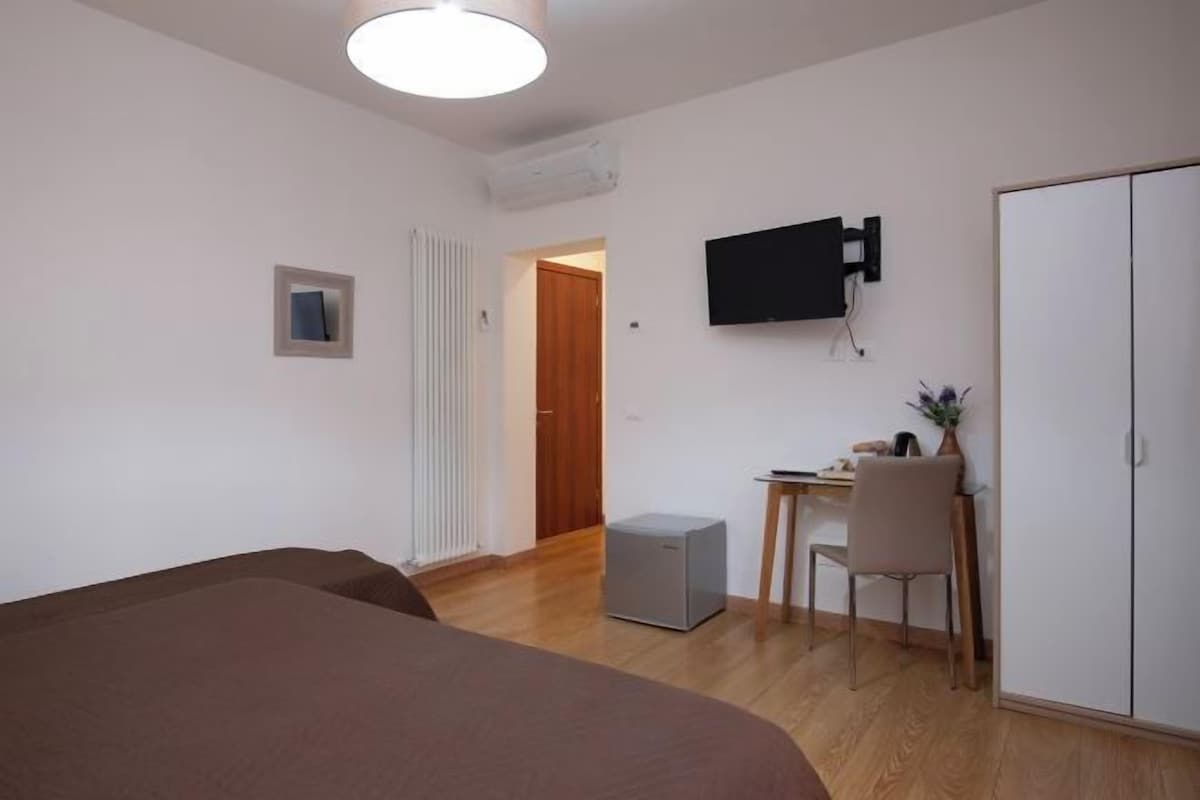 A bedroom with a bed, a desk with a chair, a TV, and a wardrobe.