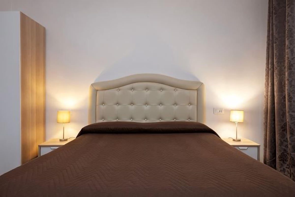 A bed with a tufted headboard, two bedside lamps, and a brown bedspread.