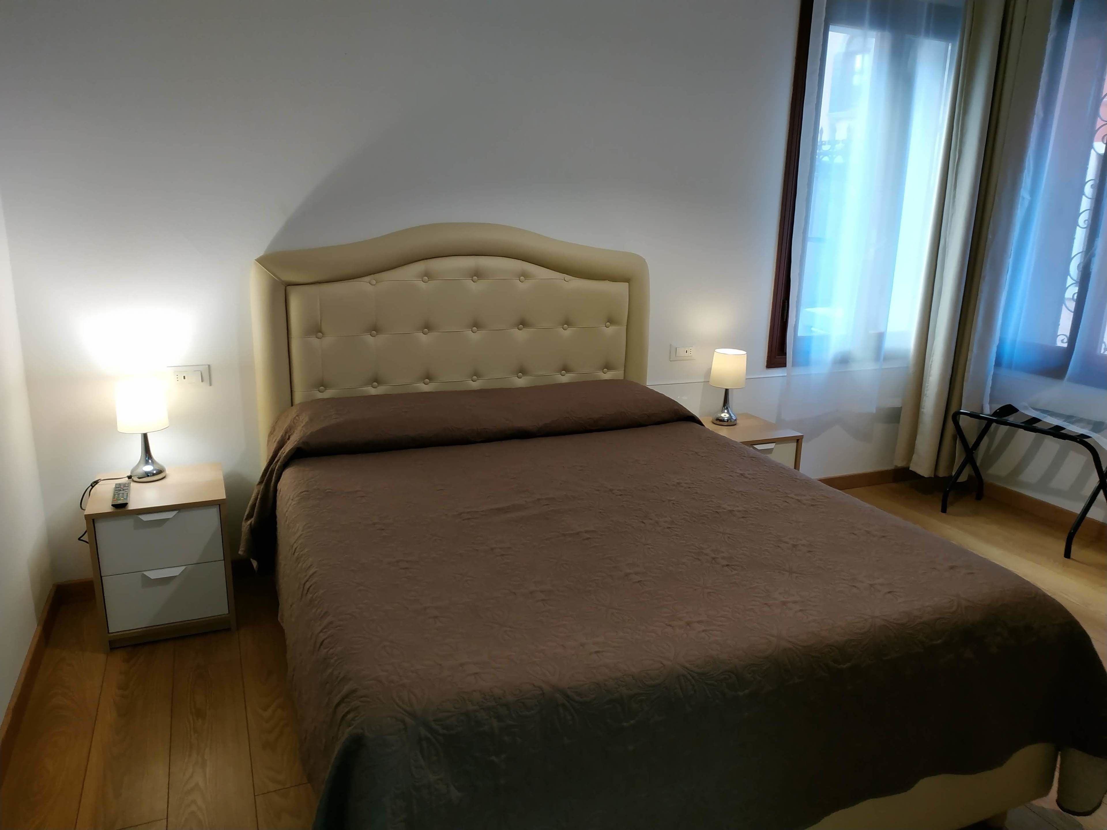 A neatly made bed with a tufted headboard, two bedside tables with lamps, and a window with curtains.