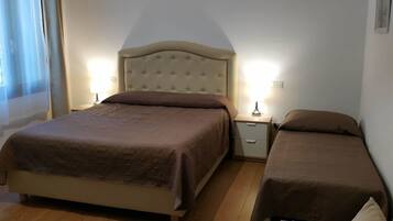 A bedroom with a large bed, a smaller bed, a chair, and a nightstand with a lamp.