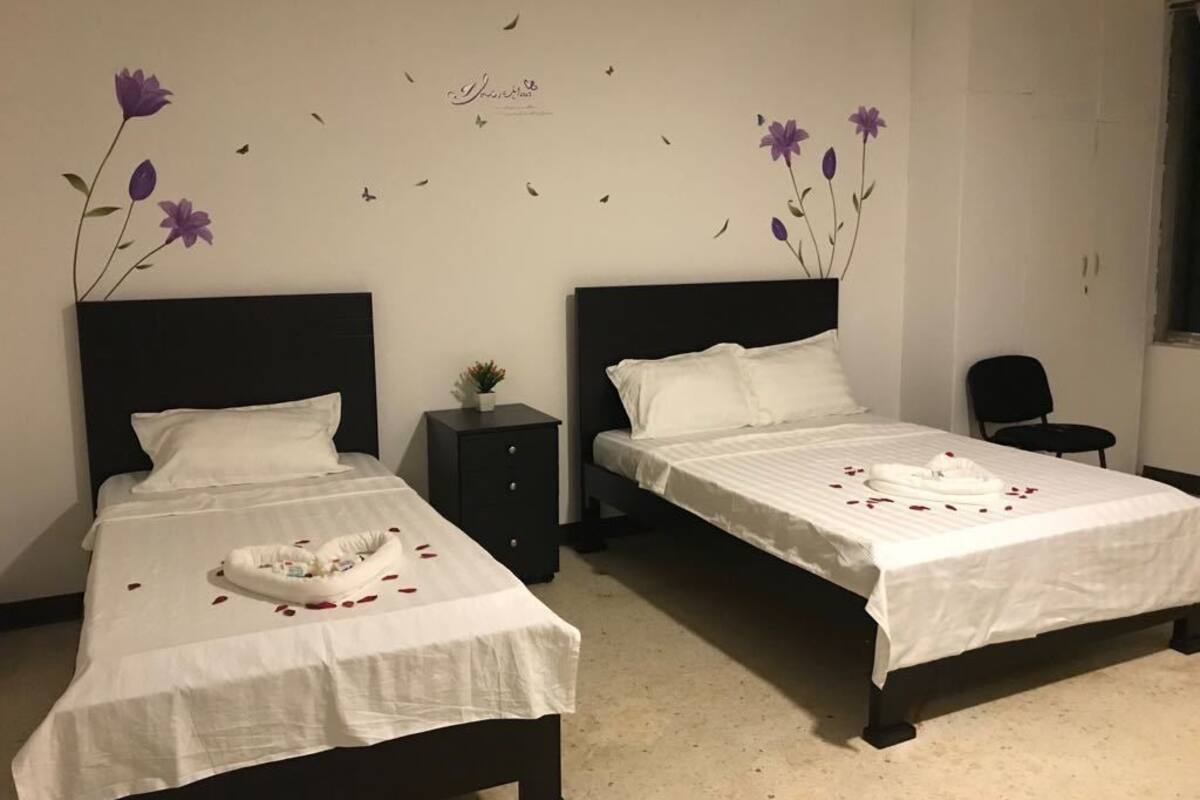 Two single beds with white linens, a small bedside table, and a wall decoration with purple flowers and butterflies.