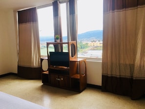 A hotel room with a view of a cityscape through large windows, a wooden entertainment unit, and a bed. - Hotel La Fortuna Roja (San José)
