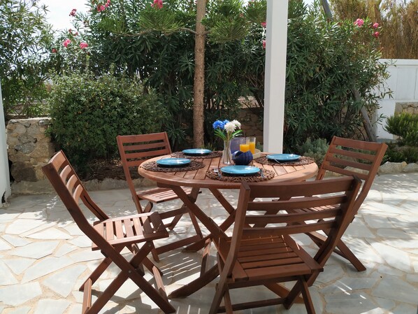 A round wooden table set for four with matching chairs, surrounded by a stone-tiled patio.