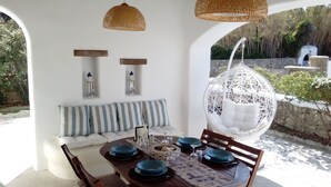 Un comedor con una mesa redonda dispuesta para cuatro personas, un banco blanco acolchado y dos faroles fijados a la pared.