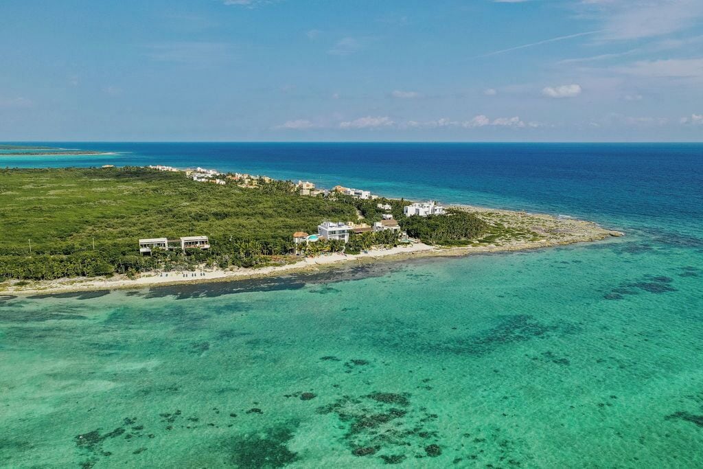 An aerial view of a coastal property with multiple buildings, a beach, and clear turquoise waters.