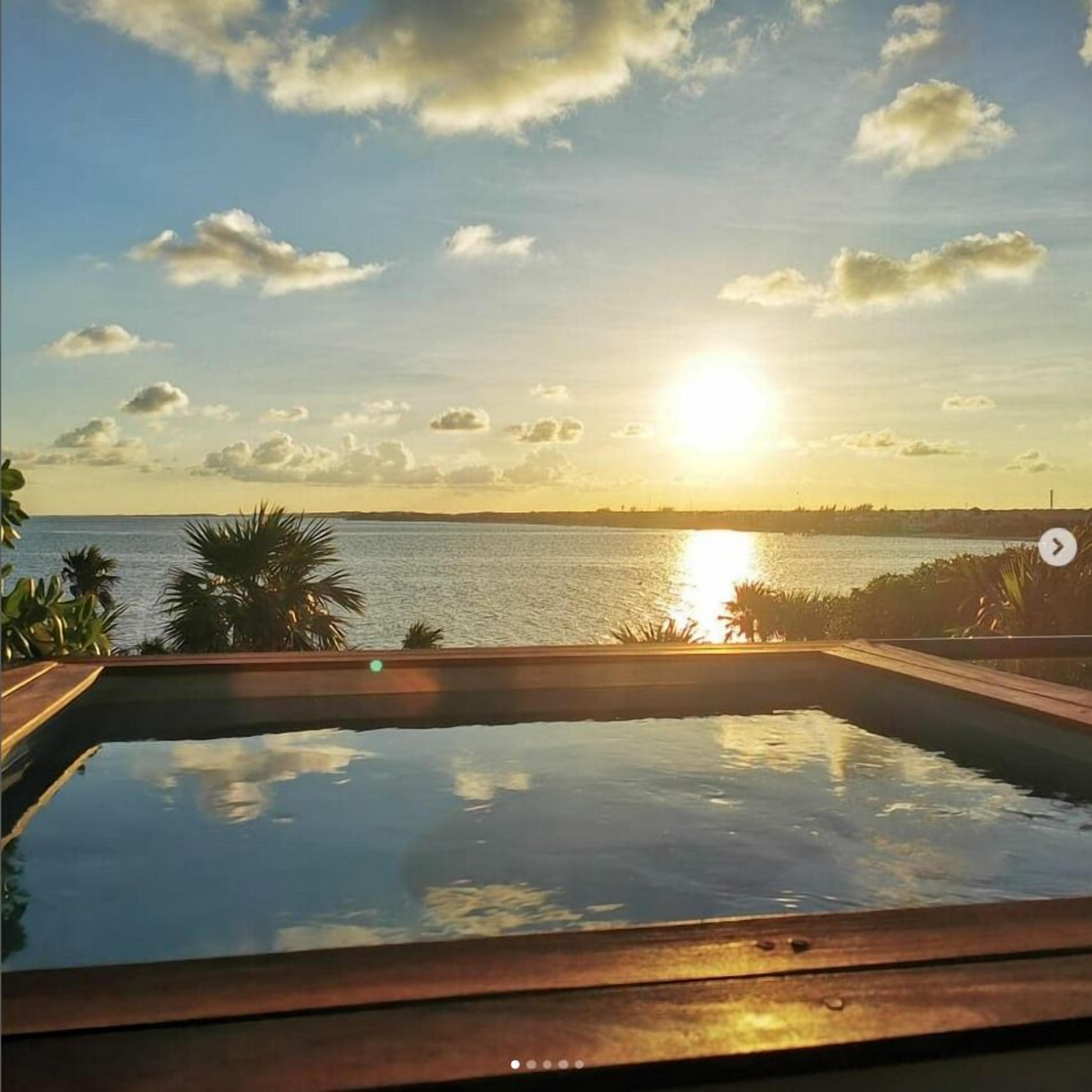 A swimming pool with a view of the sunset over water.