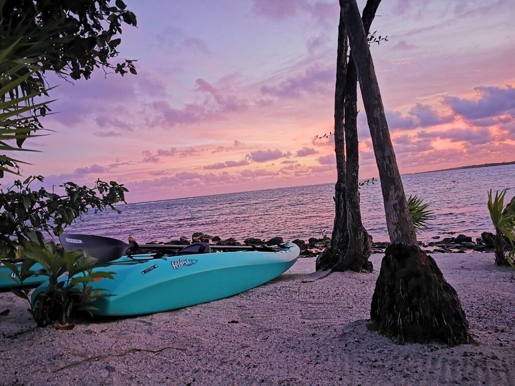 Un kayak en una playa arenosa con un atardecer de fondo.