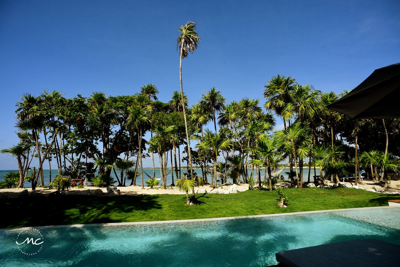 A poolside view with a clear blue sky, palm trees, and a beach in the background.