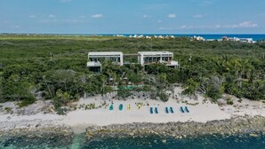 Une propriété moderne située en bord de mer, comprenant une grande maison, une piscine et une plage équipée de chaises longues.