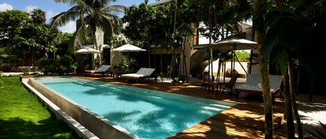 Une piscine entourée de palmiers et de verdure, avec des chaises longues et des parasols.