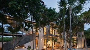 A modern house with a wooden deck, outdoor seating, and a pool. - Tulsayab Luxury Development (Tulum)