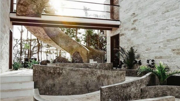 A modern interior with a curved stone structure, a staircase, and a view of the outdoors. - Tulsayab Luxury Development (Tulum)