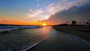 Una playa al atardecer con olas, palmeras y cielo despejado.