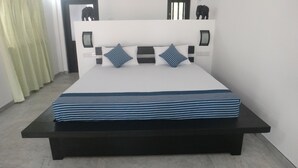 Una cama con cabecera blanca, dos mesitas de noche negras y una colcha azul a rayas.