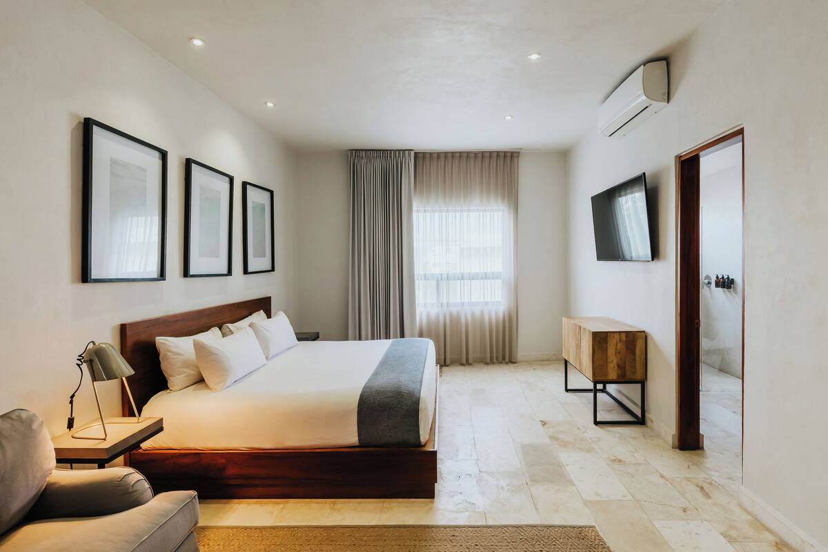 Un dormitorio moderno con una cama grande, mesitas de noche, un banco, un televisor y cuadros enmarcados en la pared.