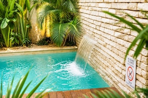 Una piscina amb cascada, envoltada de vegetació abundant i una paret de maó.
