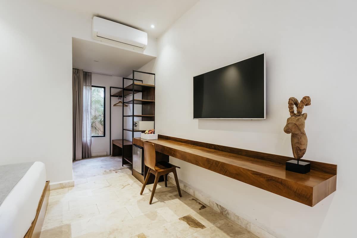 Una habitación moderna con un escritorio de madera, una silla, un televisor de pantalla plana en la pared y una pequeña escultura en un estante.