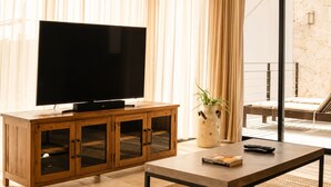 A living room with a flat-screen TV on a wooden cabinet, a coffee table with a remote and a book, and a potted plant. - The Strabon Tulum (Tulum)
