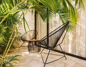 A hammock chair with a wooden seat and backrest, positioned under a palm tree in a room with a marble floor and a white curtain. - The Strabon Tulum (Tulum)
