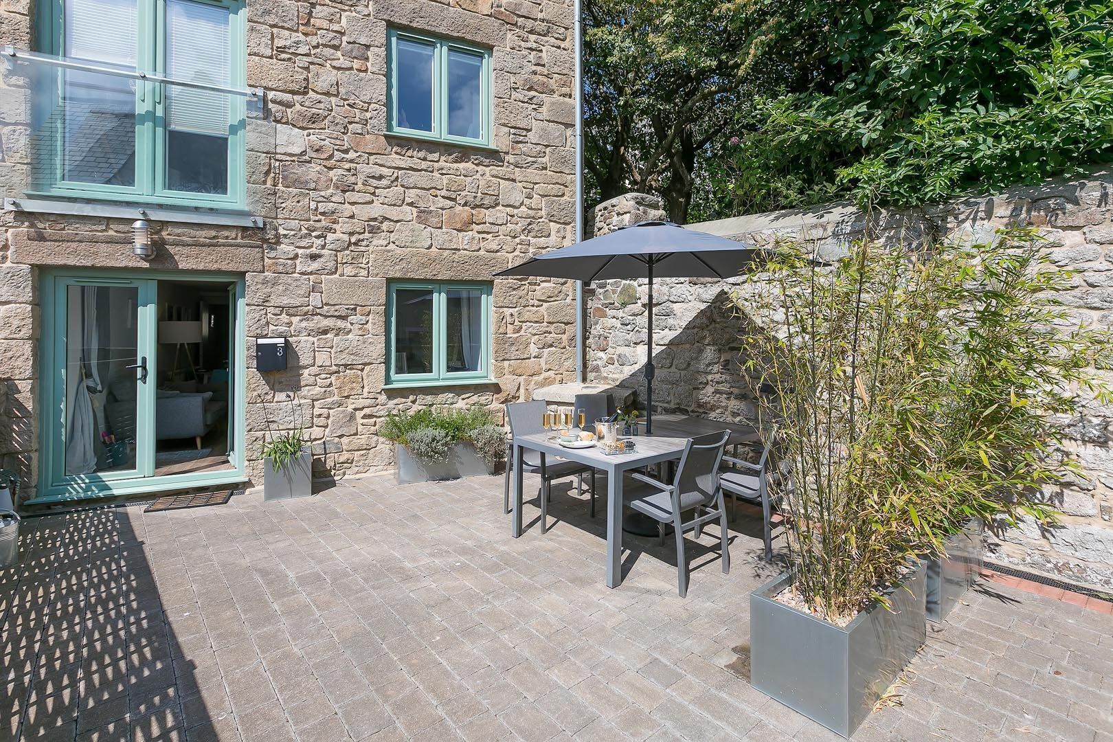 Ein Steinhaus mit einer Terrasse, die einen Tisch, Stühle, einen Blumentopf und einen Briefkasten zeigt.
