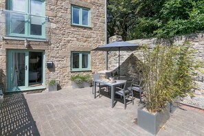 A stone building with a patio area featuring a table and chairs, a potted plant, and a mailbox.