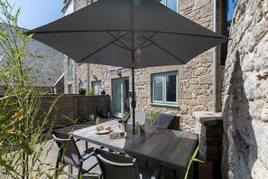 An outdoor dining area with a table and chairs, a large umbrella, and a stone building in the background.