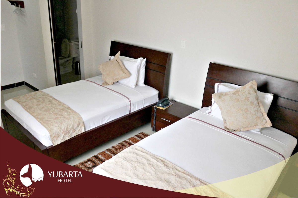 Dos camas con ropa blanca y almohadones color beige en una habitación de hotel.