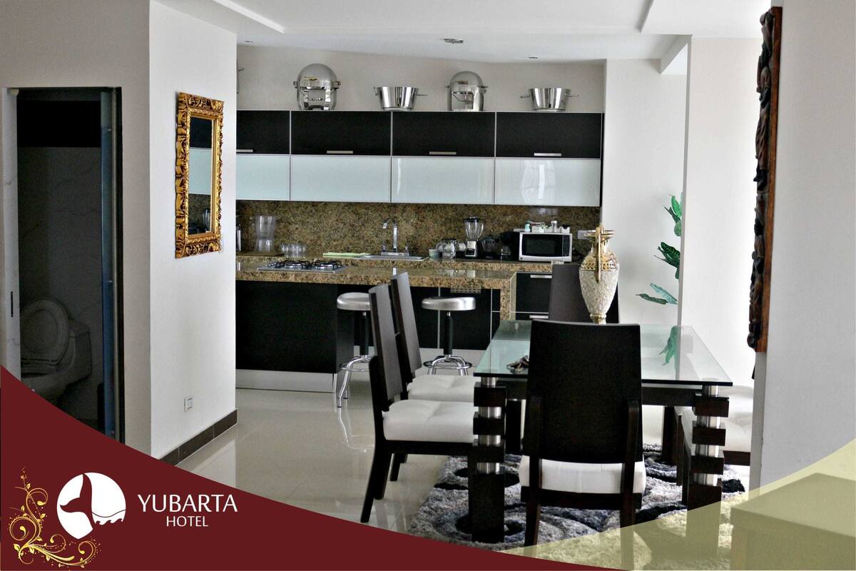 Una cocina moderna con encimeras de granito, electrodomésticos de acero inoxidable y un comedor con mesa y sillas de vidrio.