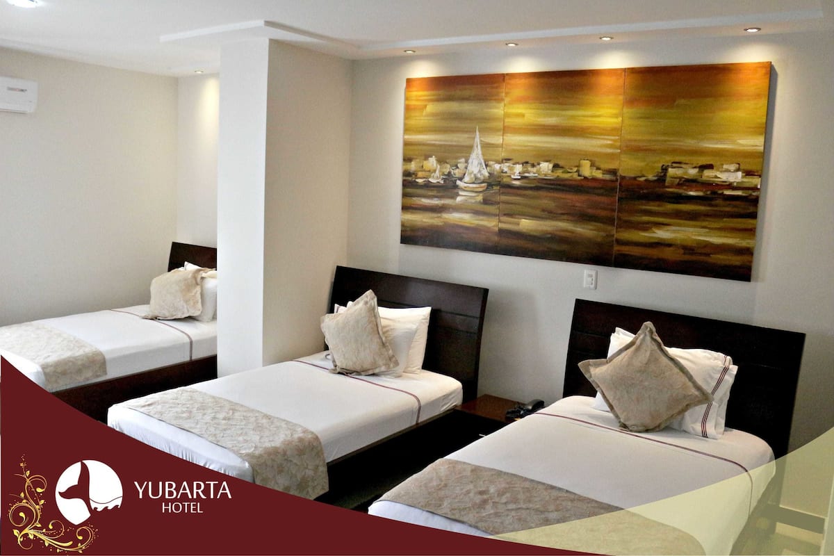 Habitación de hotel con tres camas individuales, un cuadro grande en la pared y un logotipo en la esquina inferior izquierda.