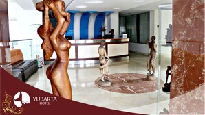 Um hall de hotel com uma mesa de recepção, um sofá e uma estátua de mulher.