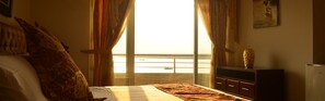 Une chambre à coucher avec un lit, une commode et une vue sur la mer grâce à de grandes fenêtres.