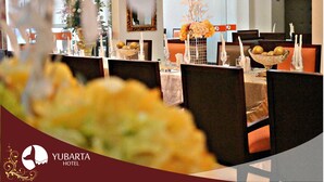 Uma área de refeições com mesas preparadas para o serviço, um espelho na parede e um vaso decorativo com flores.