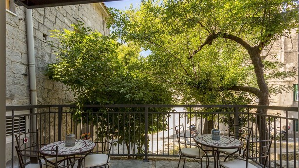 Ein Balkon mit zwei runden Tischen und vier Stühlen, umgeben von einer Steinmauer und einem Metallgeländer.